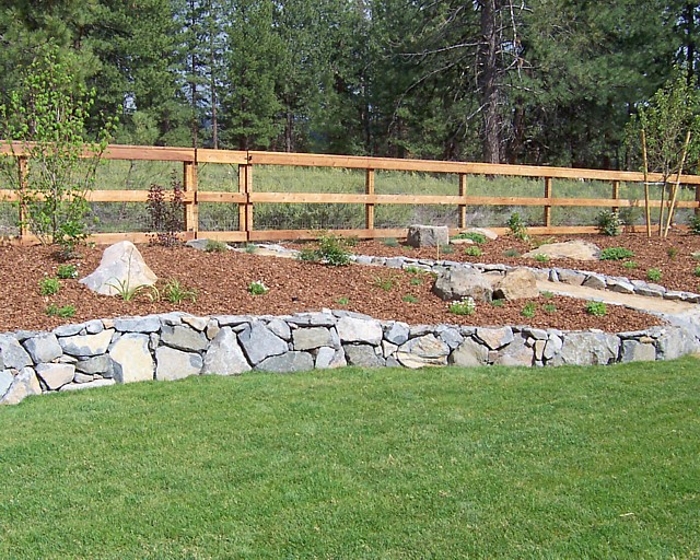 Dry stacked raised planter with redwood (3) rail ranch fence in background.